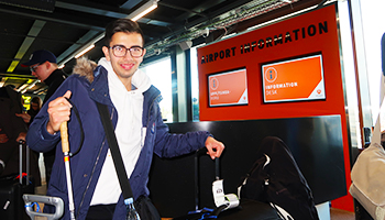 STU elev i lufthavnen, står med sin mobilitystok, foran informationsskærm